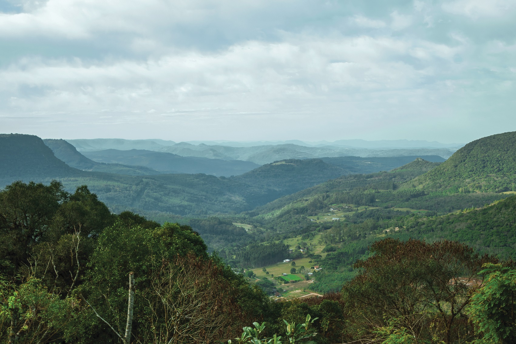 Vista do Vale do Quilombo no Belvedere, morros verdes se estendem até o horizonte, nuvens escuras cobrem o céu mas o dia está bem iluminado casas e construções aparecem espalhadas pontualmente pelos morros